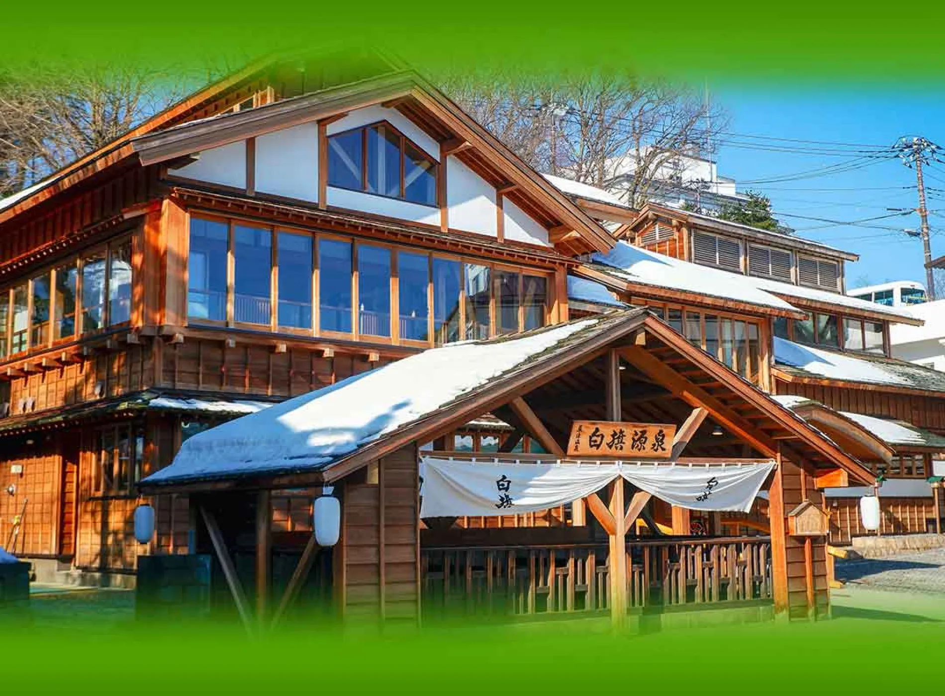 屋根に雪が積もった「白鷺源泉」の看板と白い暖簾が架かる、歴史ある風情豊かな大型木造建築の外観
