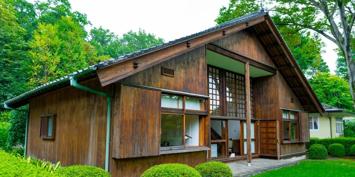 美しい緑の木々や芝生に囲まれた、大きな窓と格子戸がある趣豊かな伝統的木造住宅の外観