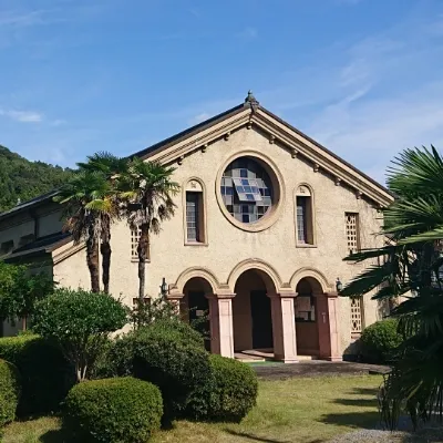 青空と山を背景に、中央の大きな丸窓と3つのアーチ状の入り口が特徴的な、洋風デザインのクラシックな木造・近代建築の外観